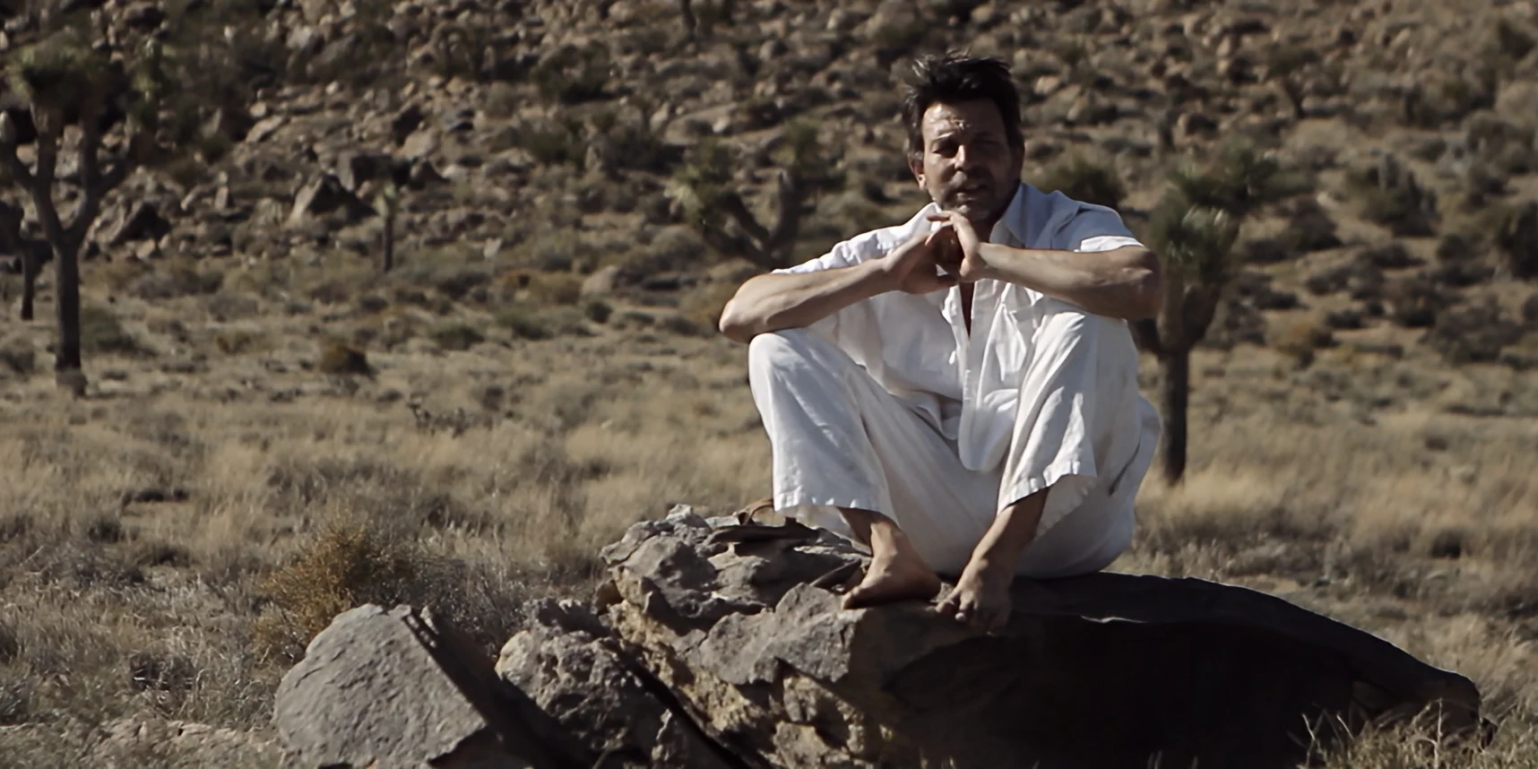 Wide shot of man sitting uneasy on large rock, gazing at Joshua Tree desert, 88 short film