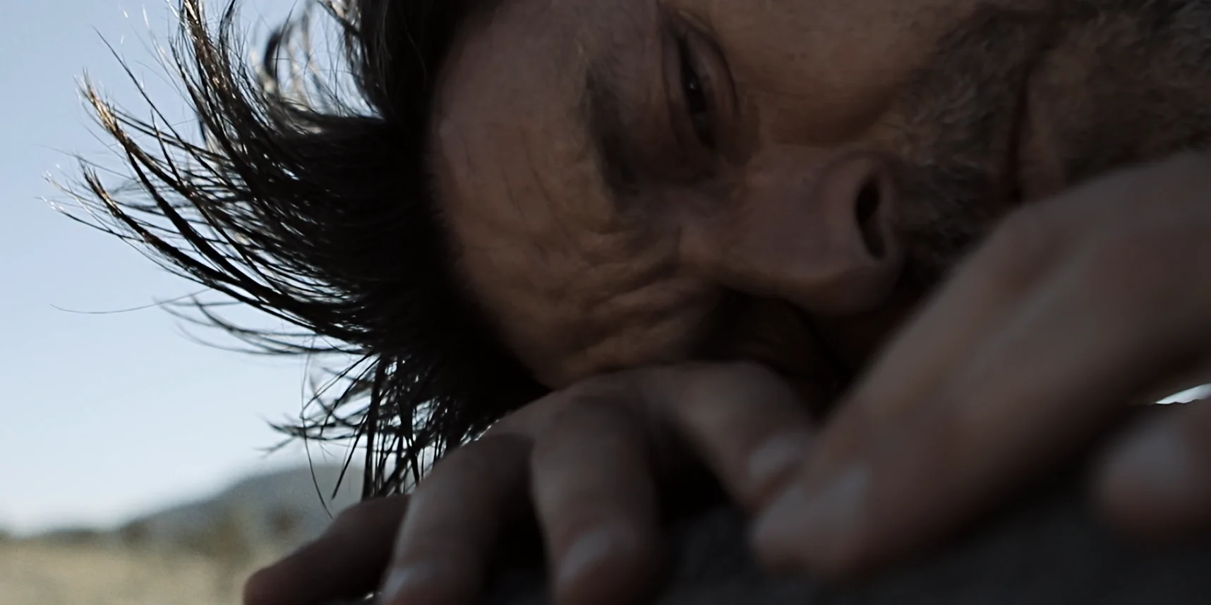 Man with empty gaze, head on hands sideways, hair in wind, sad in Joshua Tree National Park desert, 88 short film