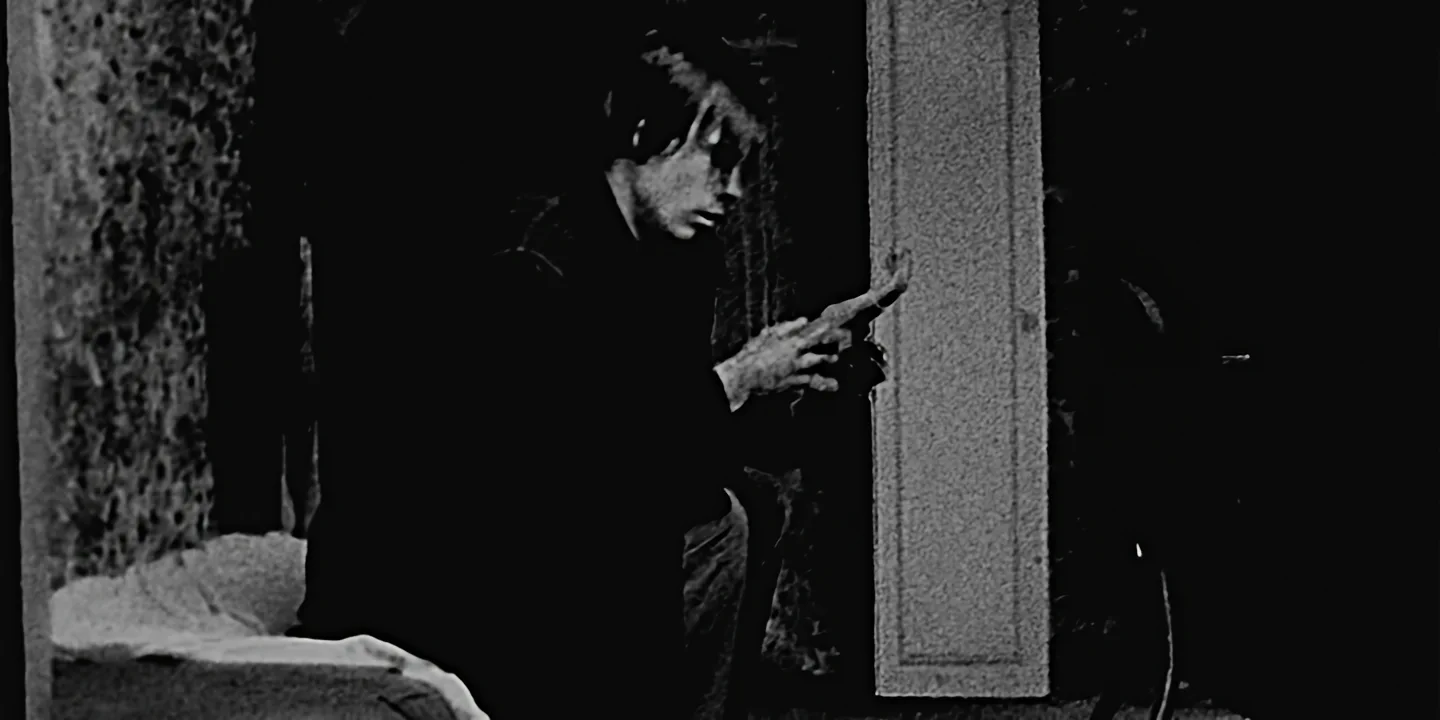 Black and white still of person in dark clothing holding severed hand in dramatic scene, The Hand short film