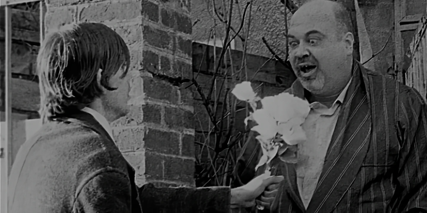 Young man offering white bouquet to old bald father-in-law smiling strangely in deserted village street, The Hand short film