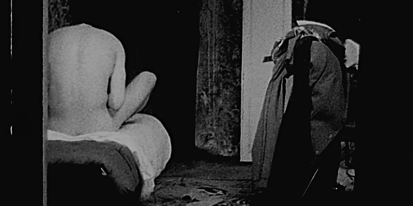 Wide shot of young man nude from back on bed in tiny dark room, The Hand short film