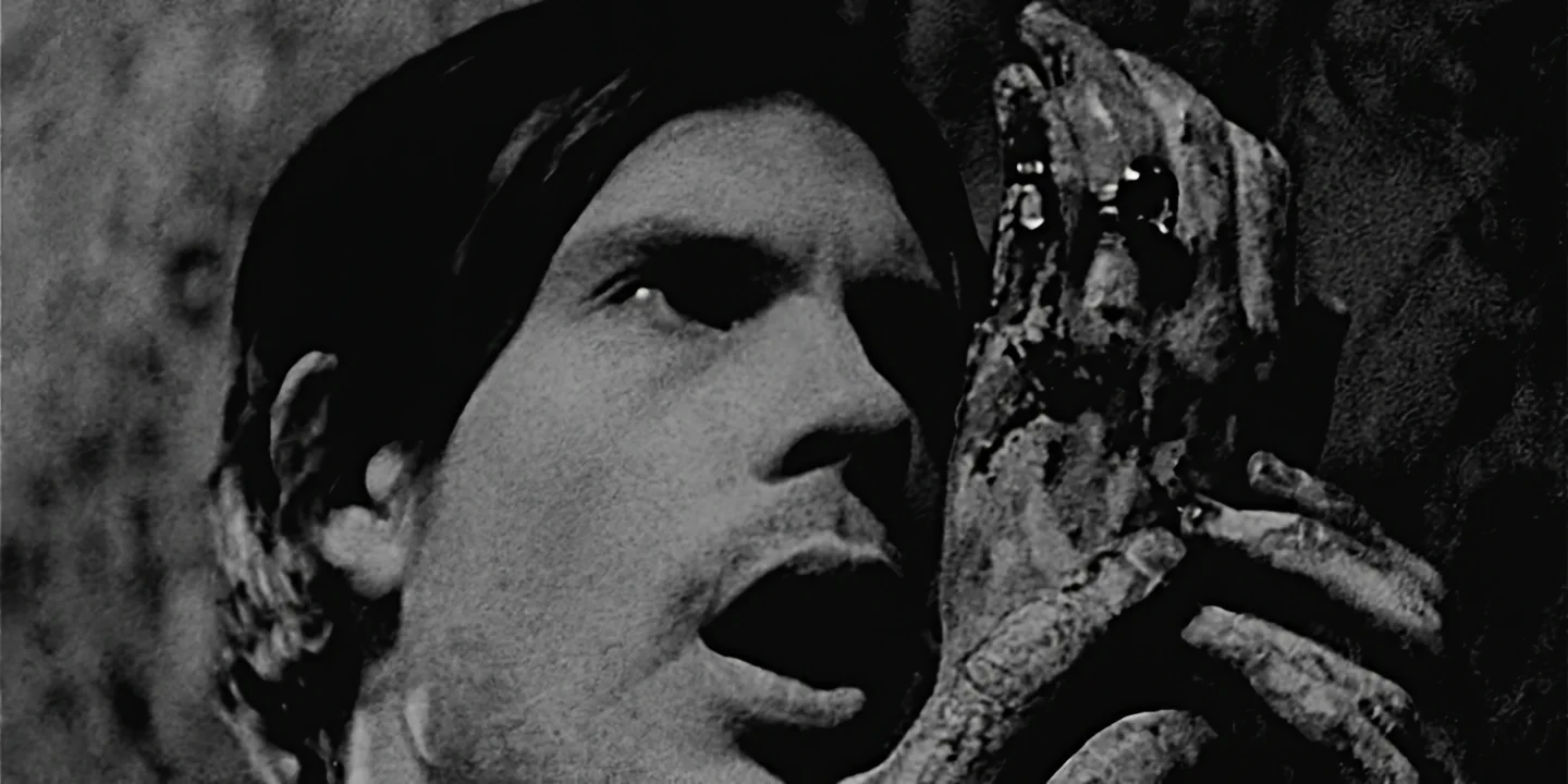 Close-up of young man holding bloody severed hand before his face in tiny basement room, The Hand short film