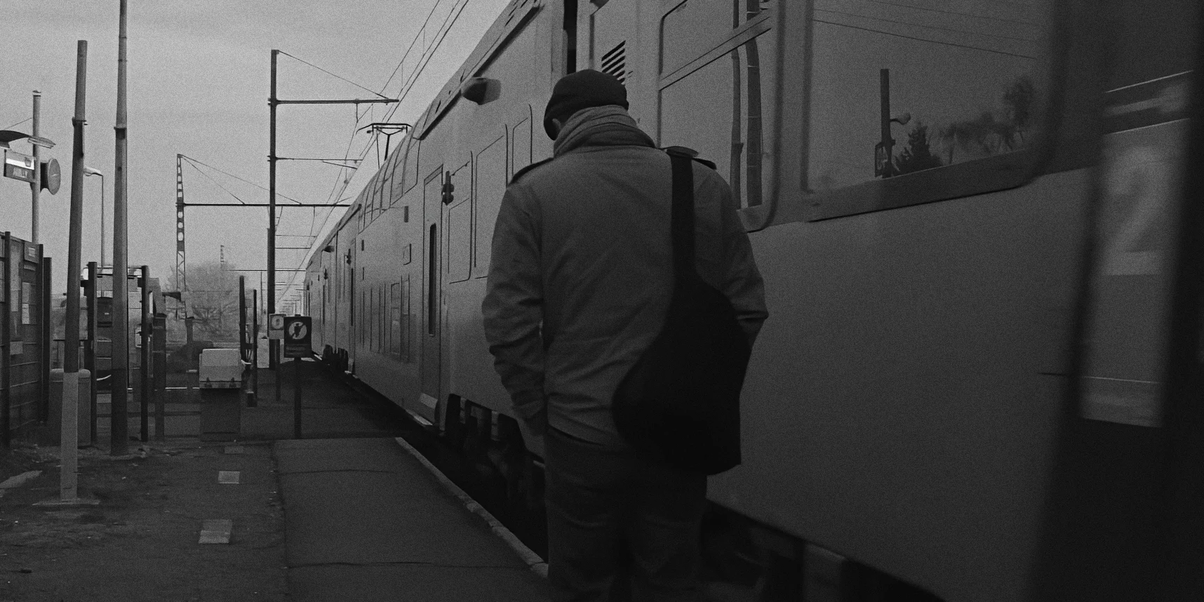 Man walking back along railway in village station, train passing beside, Twice as Far