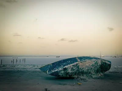 Blue hull of a boat stranded on its side at low tide, contrasting with the golden pastel sunset sky on Plage des Maristes, Dakar