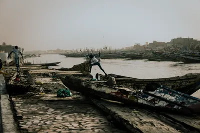 Child straddling a Lebou fishing pirogue in Saint-Louis, Senegal, with hundreds of traditional wooden boats in the background