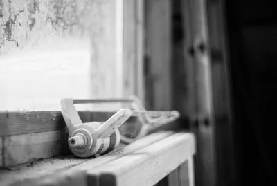 Black and white still life of a weathered, patinated vintage garden watering can in a dusty workshop, Brittany, France