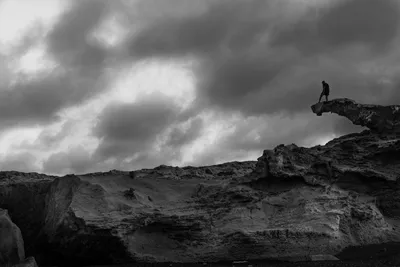 Black and white landscape at Cabo de Gata, Spain: a man's silhouette atop a rock formation under a heavy, dark sky