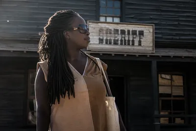Portrait of a Black woman with long red dreadlocks in profile, standing before a sheriff's office in a Western film set village, Tabernas Desert, Almería, Spain