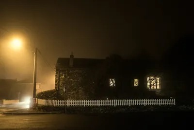 Night photo of a house with lit windows illuminated by an amber sodium streetlight in the countryside near Thiers, France