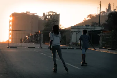 Two children roller skating on a road at sunset with the Les Mamelles lighthouse in the background, Dakar, Senegal