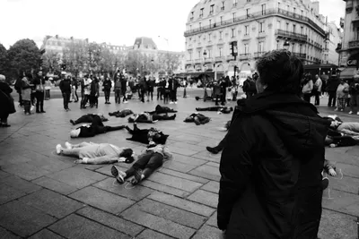 Black and white street photo of a woman observing a feminist protest with participants lying on the ground representing victims of gender-based violence, Paris, France