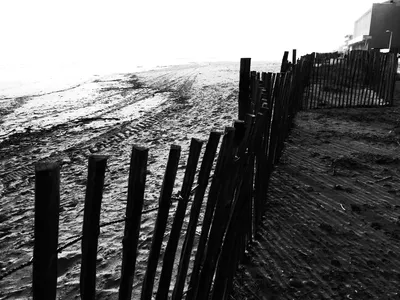 Black and white high-contrast photo of wooden beach groynes in foreground with white sea and sky in background, abstract landscape