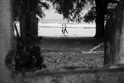 Black and white photo of an abandoned hotel on a Casamance beach, Senegal, with two people walking along the shoreline in the background