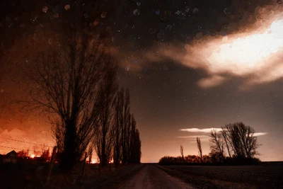 The sodium glow of a village lights up a nocturnal landscape in Beauce, France. The photograph is transformed by a textured effect, resembling droplets on the lens, creating a hybrid between reality and impression