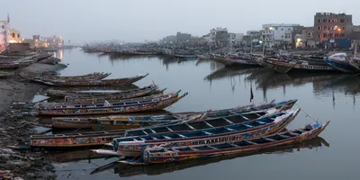 Fleet of pirogues on the Senegal River at dusk, Saint-Louis, with a bluish light and the first streetlights turning on after sunset
